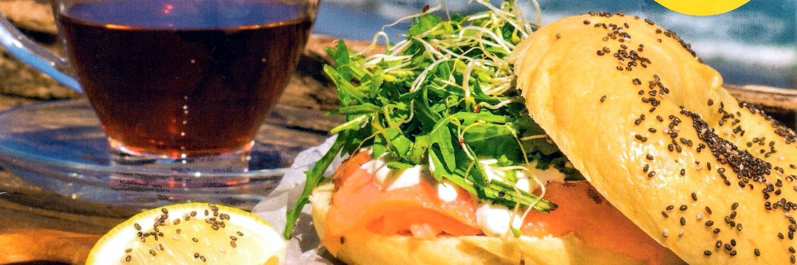 Lox and cream cheese bagel sandwich served with tea, with the ocean in the background